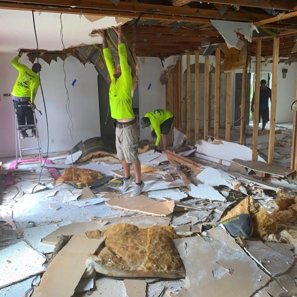 Workers removing drywall and cleaning up debris during demo in a residential room