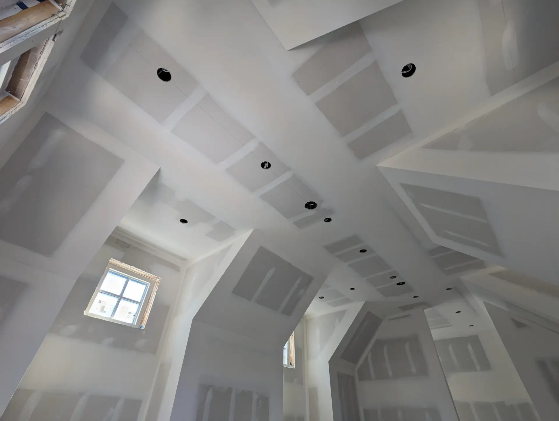 Skilled worker smoothing a compacted drywall seam at ceiling level